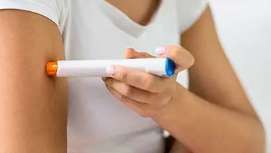 A person uses an auto-injector pen to give themselves an injection in the upper arm.