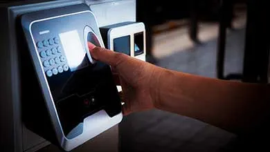Index finger pressing a wall-mounted fingerprint security scanner.