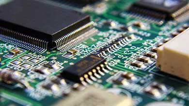 Close-up of a green circuit board with black microchips and various electronic components soldered on it.
